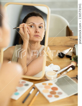 Middle-aged woman doing eyebrow make-up looking in the mirror 138578341