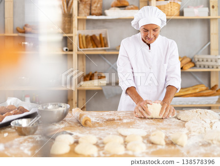 Elderly female baker kneading dough on table Elderly female baker kneading dough on table 138578396