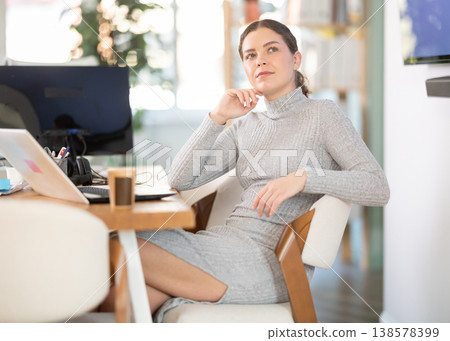 Beautiful female employee poses on armchair in modern office 138578399