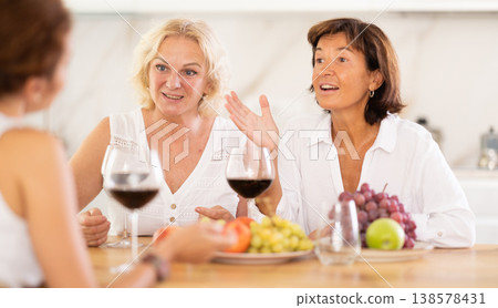 Girlfriends chatting and drinking wine at home party table Girlfriends chatting and drinking wine at home party table 138578431