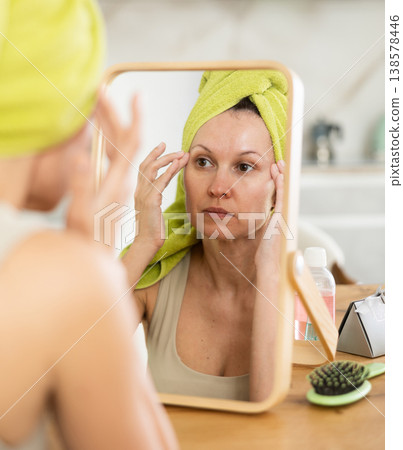 Woman with towel on head checking face in mirror after shower Woman with towel on head checking face in mirror after shower 138578446