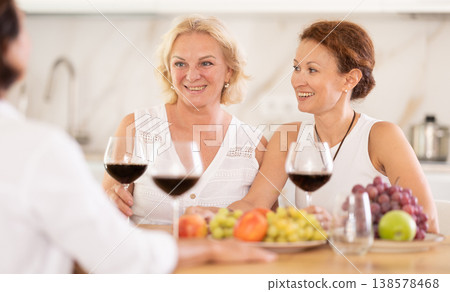Relaxed adult female friends having fun at house party, sharing stories and laughing gathered around table with wine and appetizers in kitchen Relaxed adult female friends having fun at house party, sharing stories and laughing gathered around table with wine and appetizers in kitchen 138578468