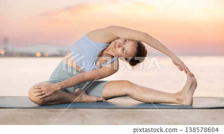 Near sea during sunset, girl performs variations of Janu Shirshasana Near sea during sunset, girl performs variations of Janu Shirshasana 138578604