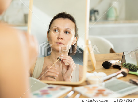 Woman applying cosmetic foundation on facial skin in front of mirror Woman applying cosmetic foundation on facial skin in front of mirror 138578627
