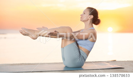 Near sea during sunset, girl performs boat pose Near sea during sunset, girl performs boat pose 138578633