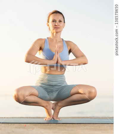 Concentrated young woman performing seated Bound Angle Pose or Butterfly Pose Baddha Konasana on seashore at sunrise Concentrated young woman performing seated Bound Angle Pose or Butterfly Pose Baddha Konasana on seashore at sunrise 138578650