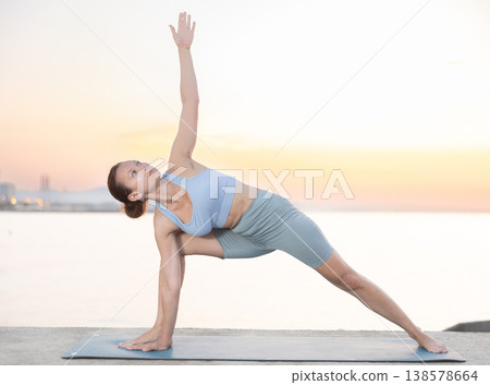 Sporty energetic female teacher doing exercises on pilates mat and demonstrating variation of warrior pose of yoga on beach at sunset. Fitness concept Sporty energetic female teacher doing exercises on pilates mat and demonstrating variation of warrior pose of yoga on beach at sunset. Fitness concept 138578664