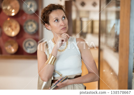 Positive woman admires the works of art on display while walking through the spacious hall of museum 138578667