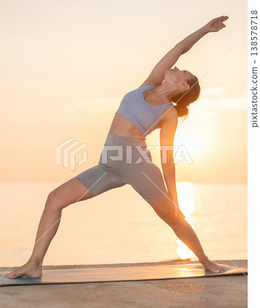 Near sea during sunset, girl performs variations of virabhadrasana Near sea during sunset, girl performs variations of virabhadrasana 138578718