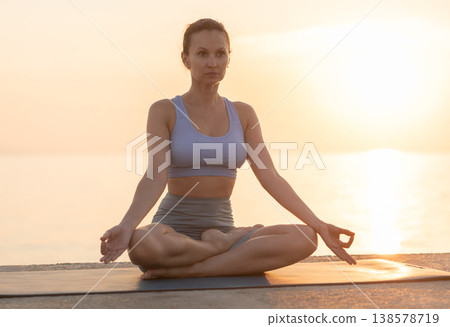 Happy slim woman making yoga meditation in lotus pose on beach at sunrise 138578719