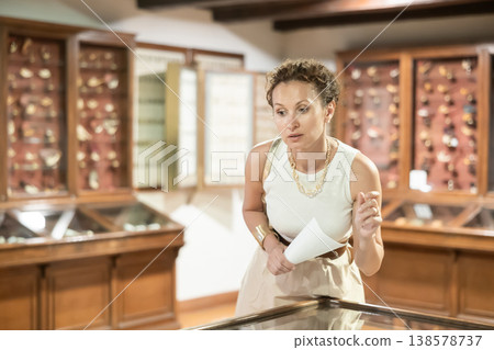 Woman with sheet piece of paper in her hands walks around museum hall Woman with sheet piece of paper in her hands walks around museum hall 138578737