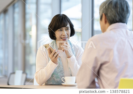 一位六十多歲的婦女在咖啡館裡用智慧型手機通話。 一位六十多歲的婦女在咖啡館裡用智慧型手機通話。 138578821