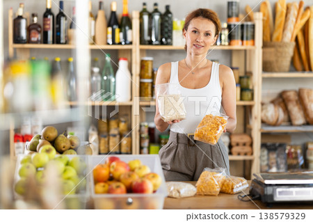 Friendly female salesperson offers to buy oat flakes and cornflakes in produce section of supermarket 138579329
