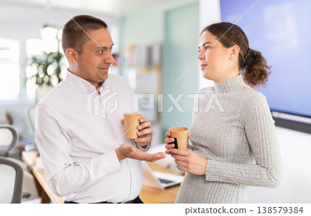 Two office workers drink coffee and chat during work break Two office workers drink coffee and chat during work break 138579384