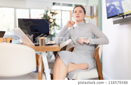 Beautiful female employee poses on armchair in modern office Beautiful female employee poses on armchair in modern office 138579386