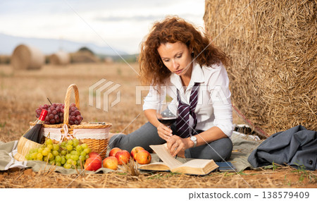 Woman in white blouse and suit spends time in field, settled down in nature with book and drink Woman in white blouse and suit spends time in field, settled down in nature with book and drink 138579409