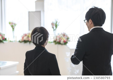 喪親家屬的背影和在葬禮現場接受指示的工作人員。 喪親家屬的背影和在葬禮現場接受指示的工作人員。 138580793