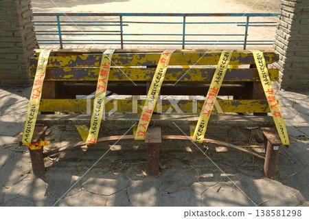 An old wooden park bench wrapped in caution tape. An old wooden park bench wrapped in caution tape. 138581298
