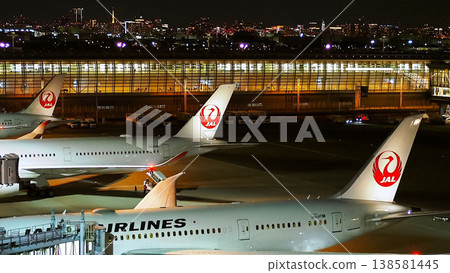 Haneda Airport terminal at night, lined with JAL passenger planes. 138581445