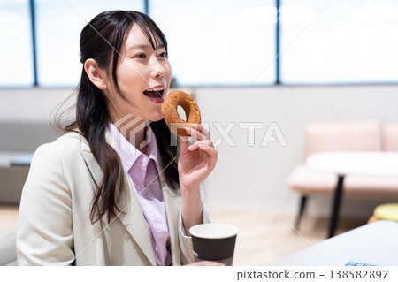一位女士在工作間隙，一邊喝咖啡一邊吃甜甜圈，放鬆身心。 138582897