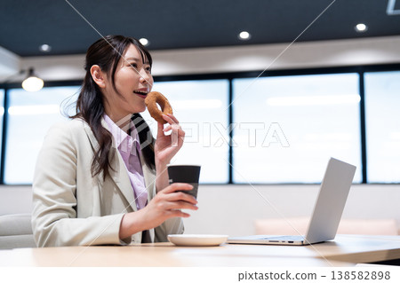 一位女士在工作間隙,一邊喝咖啡一邊吃甜甜圈,放鬆身心。 一位女士在工作間隙,一邊喝咖啡一邊吃甜甜圈,放鬆身心。 138582898