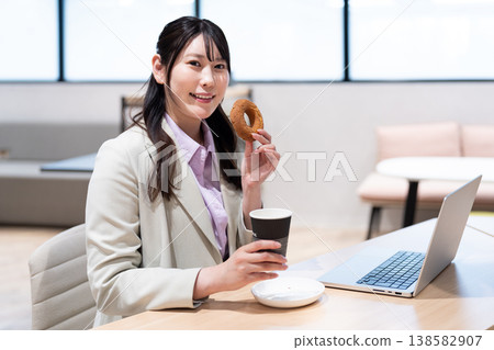 一位女士在工作間隙，一邊喝咖啡一邊吃甜甜圈，放鬆身心。 138582907