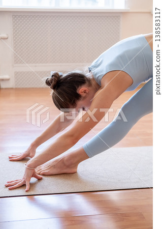 Woman fitness. Stretching exercise. Athlete bending in yoga split pose training hamstrings back muscle on wooden floor in fitness studio. Woman fitness. Stretching exercise. Athlete bending in yoga split pose training hamstrings back muscle on wooden floor in fitness studio. 138583117