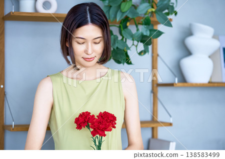 母親節禮物。一位年輕的日本女子溫柔地凝視著一朵紅色的康乃馨。 母親節禮物。一位年輕的日本女子溫柔地凝視著一朵紅色的康乃馨。 138583499