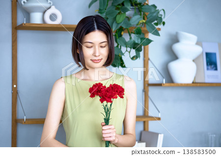 一位日本女性手持紅色康乃馨,面帶微笑——這是母親節的象徵。 一位日本女性手持紅色康乃馨,面帶微笑——這是母親節的象徵。 138583500