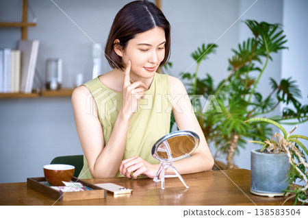 一位微笑的女士對著鏡子檢查自己的皮膚狀況。美容、護膚、生活方式。 一位微笑的女士對著鏡子檢查自己的皮膚狀況。美容、護膚、生活方式。 138583504