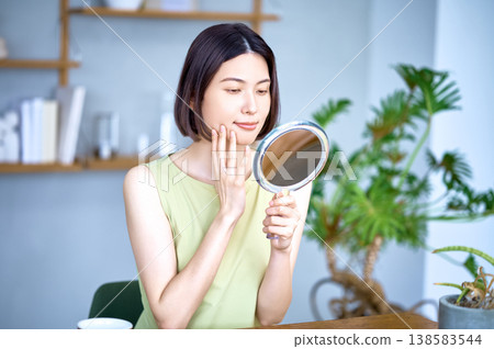一位擁有完美肌膚的日本女性正在鏡子前檢查自己的皮膚狀況。護膚圖片。 138583544