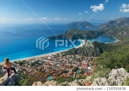 Young woman looking at Oludeniz beach, blue lagoon with clear bright turquoise water, Lycia coast. Summer day walk by Lycian way at family vacation in Mediterranean Sea, Fethye, Antalya region, Turkey Young woman looking at Oludeniz beach, blue lagoon with clear bright turquoise water, Lycia coast. Summer day walk by Lycian way at family vacation in Mediterranean Sea, Fethye, Antalya region, Turkey 138583636