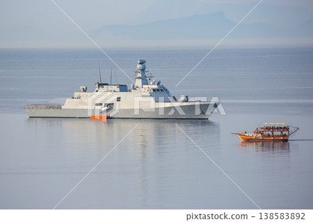 Naval ship and boat on calm water near coastline during daylight hours in tropical region 138583892