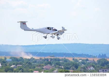 Light aircraft flying over green landscape near small houses on a sunny day Light aircraft flying over green landscape near small houses on a sunny day 138583894