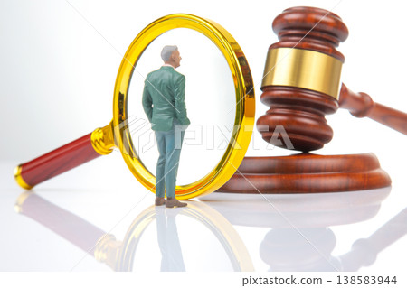 Miniature people examine a magnifying glass next to a gavel in a legal setting during the daytime 138583944