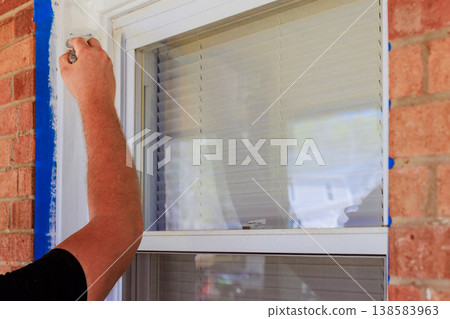 Painter is using brush to paint window frame near brick wall during home renovation setting. Painter is using brush to paint window frame near brick wall during home renovation setting. 138583963