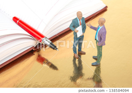 Miniature figurines of two people talking near an open notebook with a pen on a reflective surface Miniature figurines of two people talking near an open notebook with a pen on a reflective surface 138584094