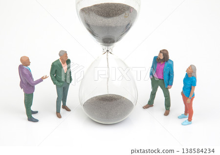 Miniature people gather around an hourglass to discuss time and decisions in a simple setting Miniature people gather around an hourglass to discuss time and decisions in a simple setting 138584234