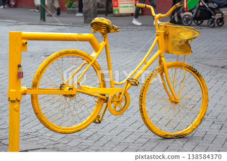 Unique yellow bicycle parked on street in urban area during daytime near shops and pedestrians Unique yellow bicycle parked on street in urban area during daytime near shops and pedestrians 138584370