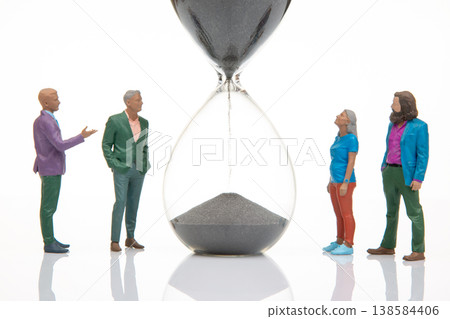Miniature people gather around an hourglass discussing time and its significance in a creative  138584406