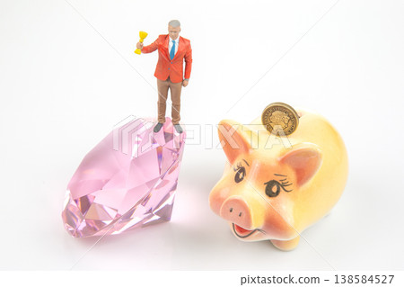 Miniature people hold a trophy and stand on diamond while other miniature figure sits on a piggy 138584527
