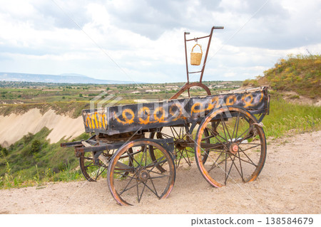 Old cart rests on hills overlooking a valley with green fields and distant mountains on a cloudy day Old cart rests on hills overlooking a valley with green fields and distant mountains on a cloudy day 138584679