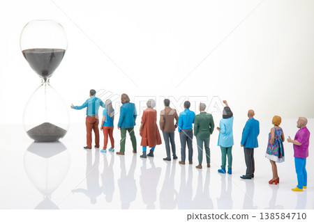 Miniature people waiting for time to pass near a large hourglass in a simple indoor space Miniature people waiting for time to pass near a large hourglass in a simple indoor space 138584710