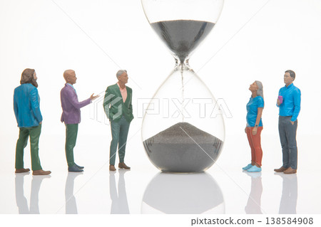 Miniature people gather around hourglass to discuss the passage of time and its impact on their Miniature people gather around hourglass to discuss the passage of time and its impact on their 138584908