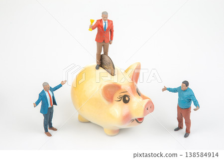 Miniature people around a piggy bank show teamwork and joy with one standing on top holding a trophy 138584914