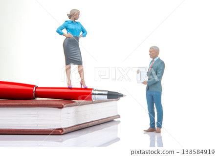 Miniature figurines of man and woman on a book with a pen at an office setting during daytime Miniature figurines of man and woman on a book with a pen at an office setting during daytime 138584919