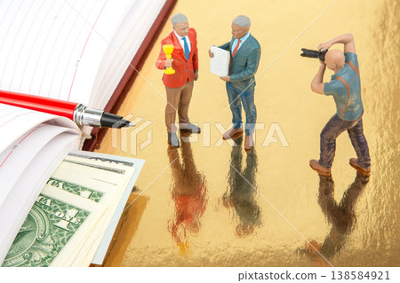 Miniature figurines of people in a business conversation with money on the table and a photographer Miniature figurines of people in a business conversation with money on the table and a photographer 138584921