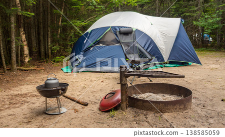 Camping scene featuring a large tent set up in a forested area with a fire pit and grill nearby on a sandy ground Camping scene featuring a large tent set up in a forested area with a fire pit and grill nearby on a sandy ground 138585059
