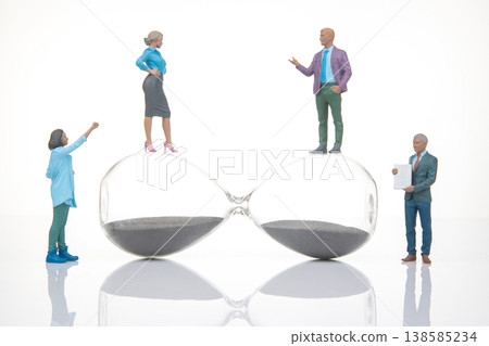 Miniature people interact on hourglass while discussing time management in a staged setting Miniature people interact on hourglass while discussing time management in a staged setting 138585234