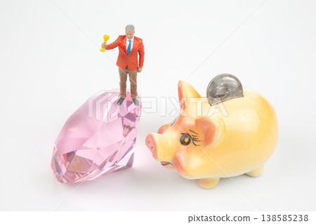 Miniature people celebrate success with trophies and financial goals near a piggy bank Miniature people celebrate success with trophies and financial goals near a piggy bank 138585238